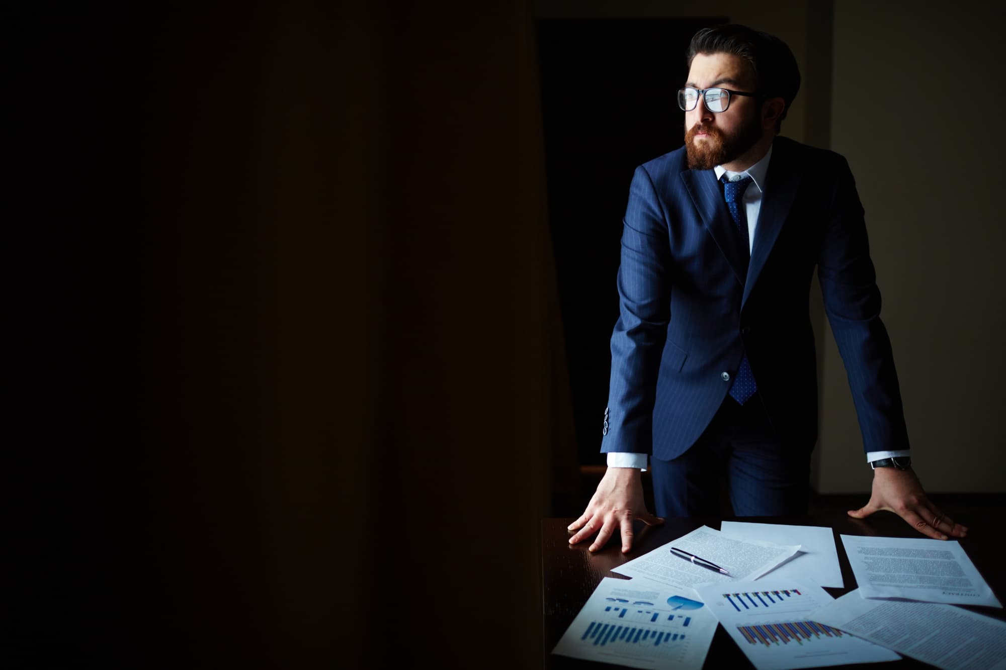 Homem de terno analisando documentos e gráficos sobre uma mesa